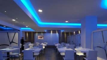 A modern restaurant with a blue-lit ceiling and white tables and chairs.