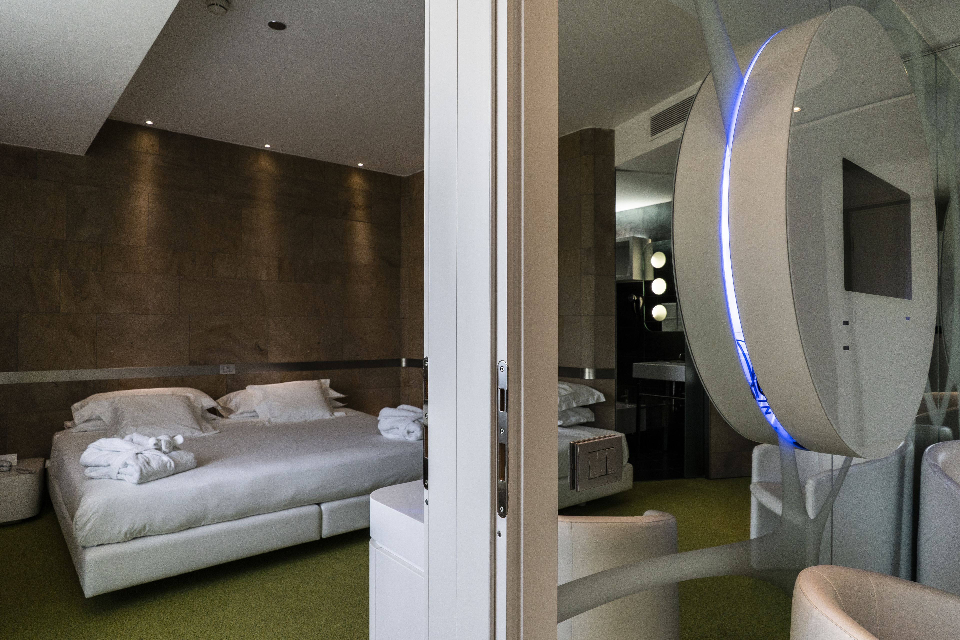 Ein modernes Hotelzimmer mit einem großen Bett, einem Nachttisch, einem Spiegel und einem Badezimmer mit Dusche und Toilette.