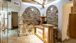 Un espace bar aux murs de pierre, avec un comptoir et des tabourets en bois, un sol en pierre et une enseigne sur laquelle on peut lire « Isanera ».