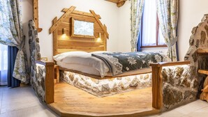 Une chambre à coucher au style rustique, avec une tête de lit en bois, un mur en pierre et un lit recouvert d’une couvre-lit à motifs floraux.