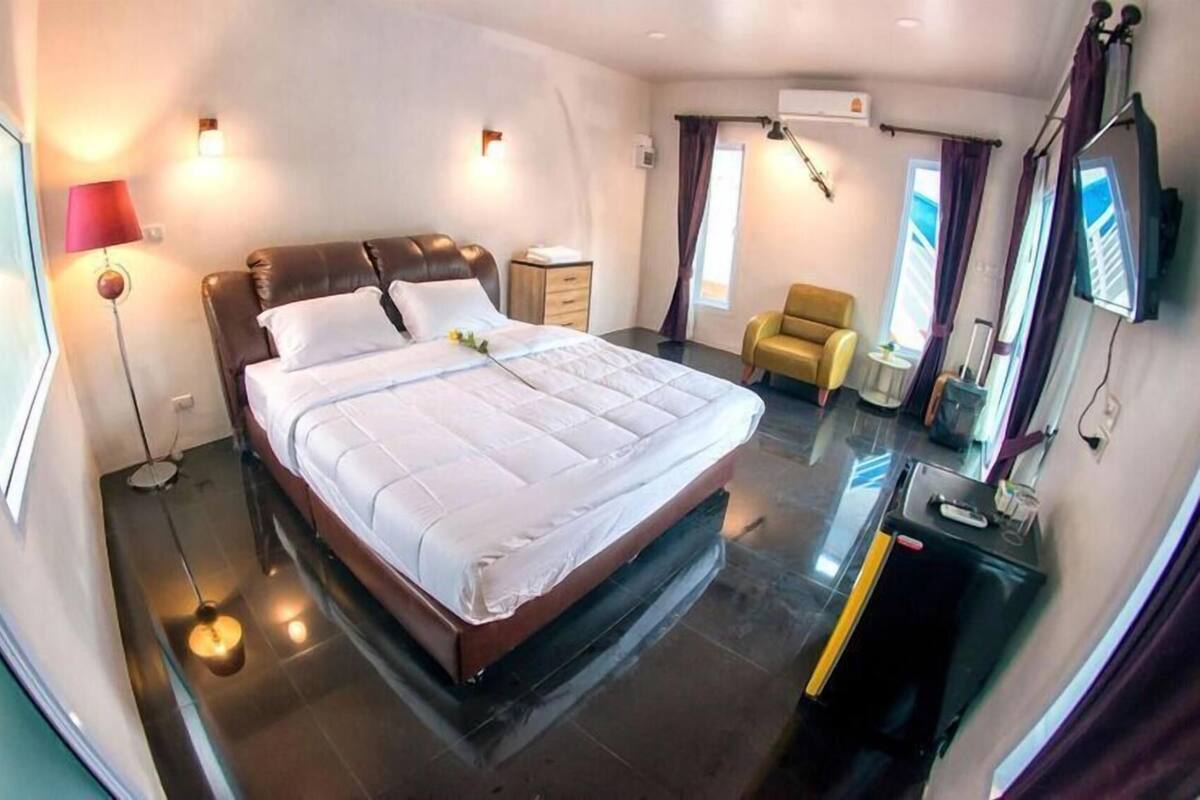 Ein Hotelzimmer mit einem großen Bett, Nachttischen, einem Sessel, einem Fernseher und einer Klimaanlage.