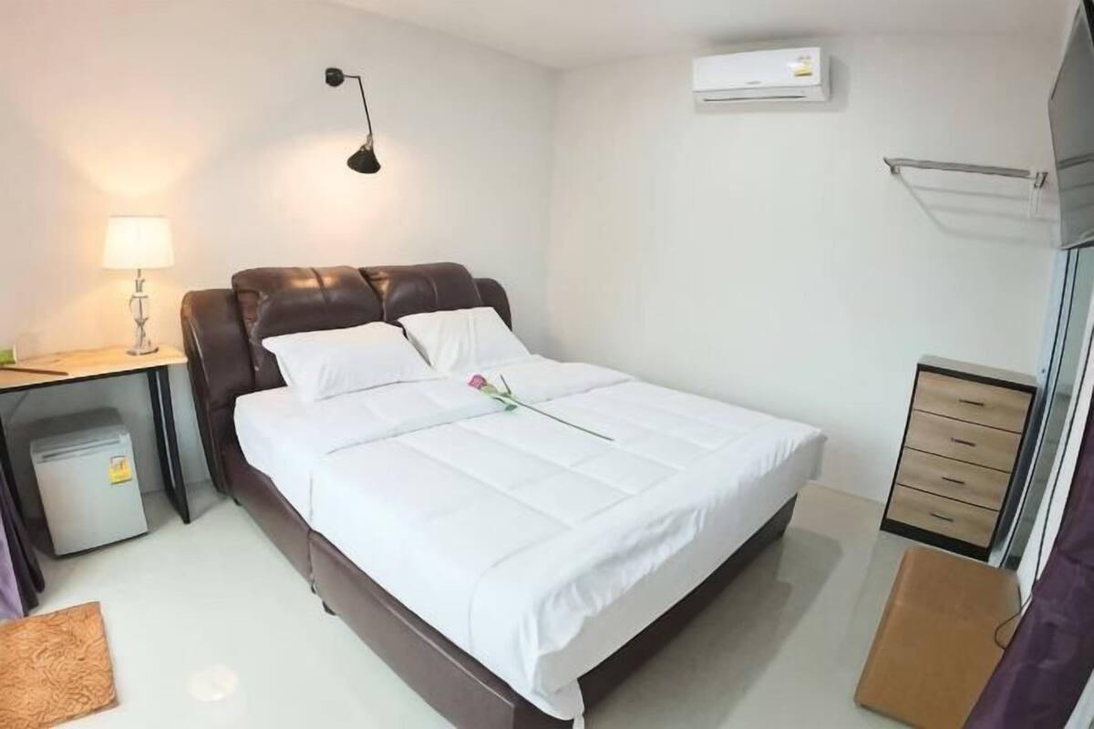 Ein ordentlich eingerichtetes Hotelzimmer mit Bett, Nachttisch, Lampe und kleinem Papierkorb.
