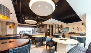 Ein modernes Restaurant mit runden Tischen, blau gepolsterten Stühlen und einer zentralen Barinsel.