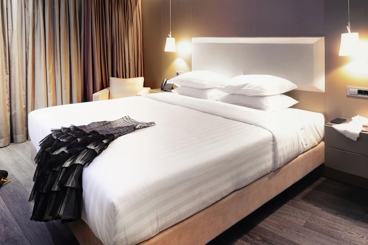 Hotellihuone, jossa on suuri sänky, yöpöytä lampun kanssa ja puhelin.