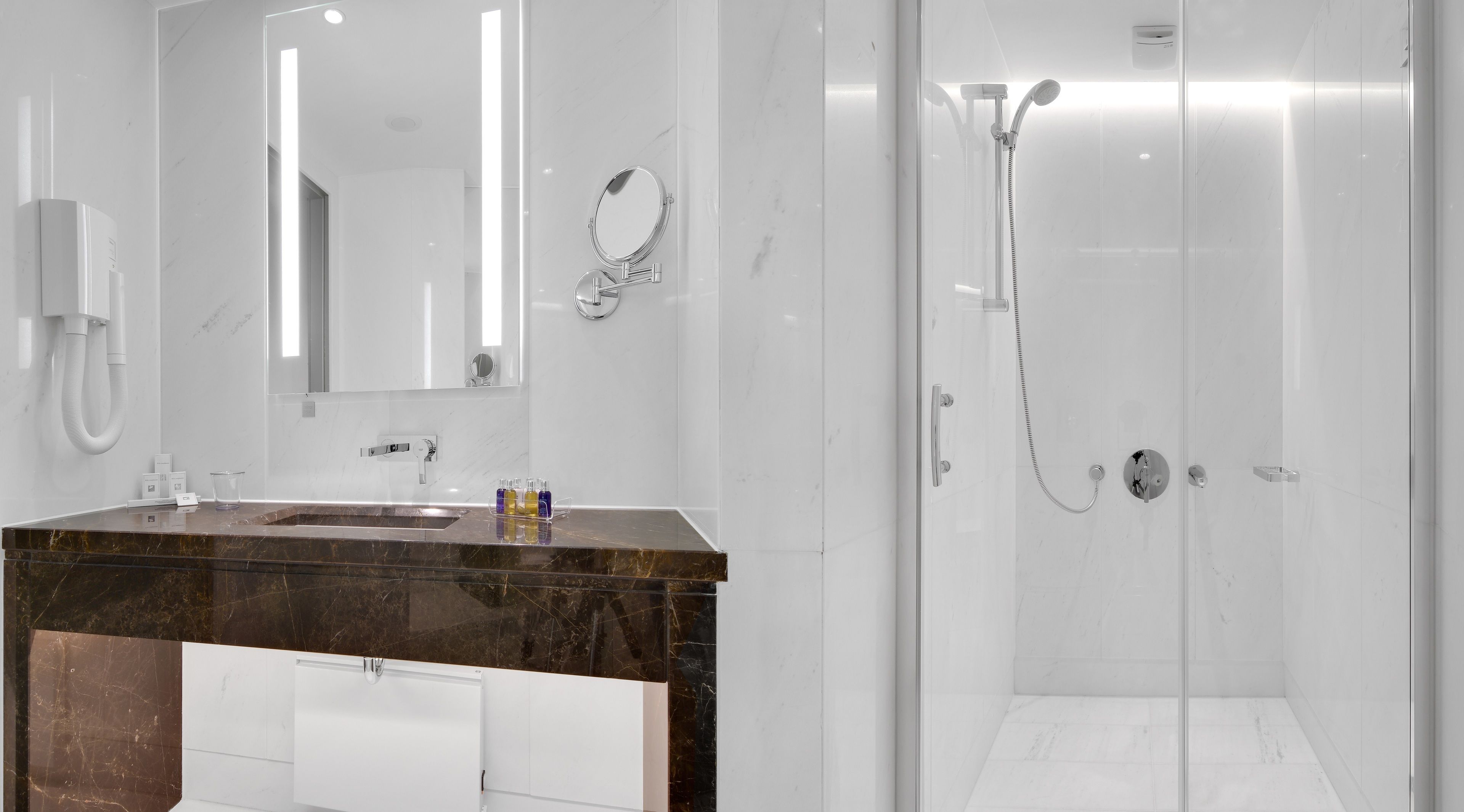 A modern bathroom with a marble sink, a large mirror, and a glass-enclosed shower area.