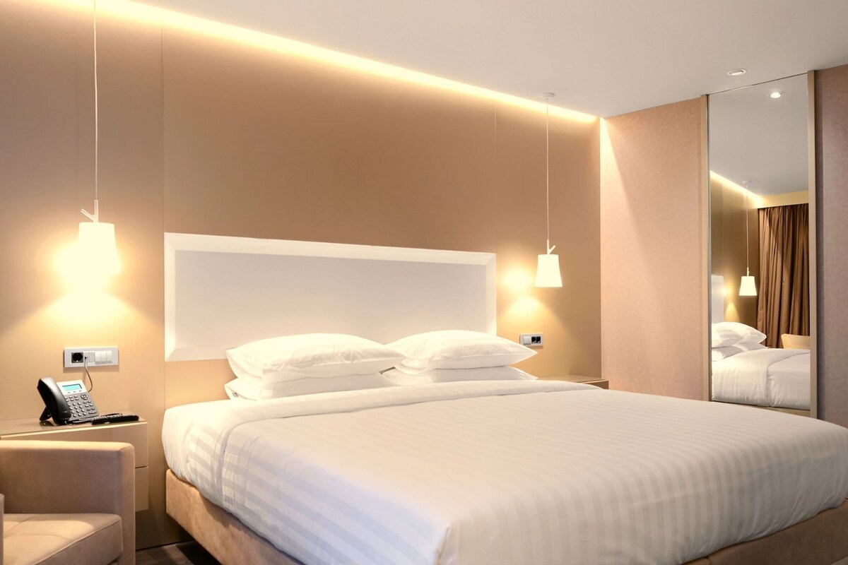 Een moderne hotelkamer met een groot bed, nachtlampjes, een telefoon en een spiegel.