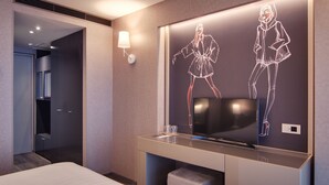 Une chambre d’hôtel moderne dotée d’un grand miroir qui reflète une œuvre d’art numérique, d’un téléviseur à écran plat et d’une table de chevet surmontée d’un récipient en verre.