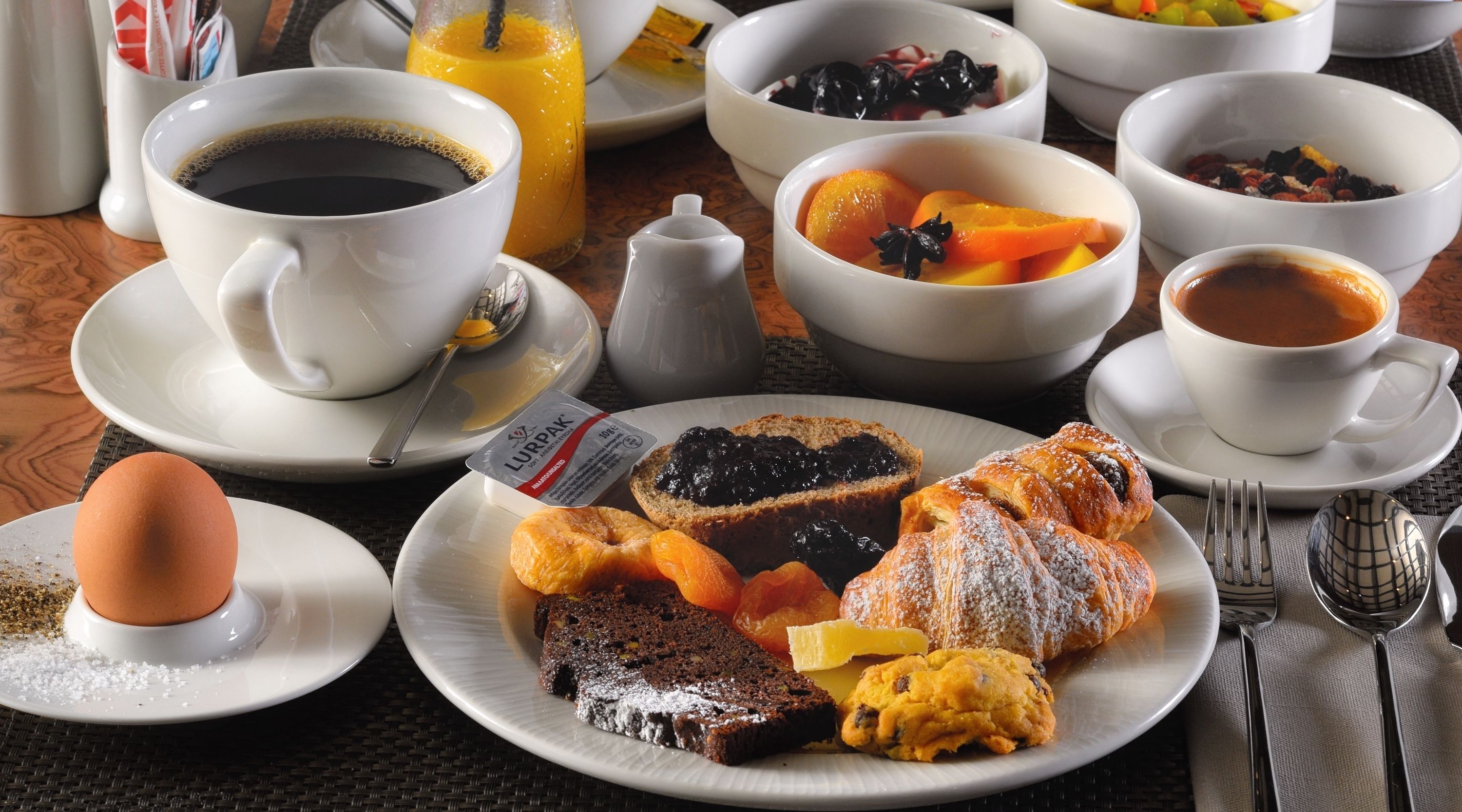 Ein Frühstückstisch mit Kaffee, Saft und verschiedenen Gebäcken auf Tellern.