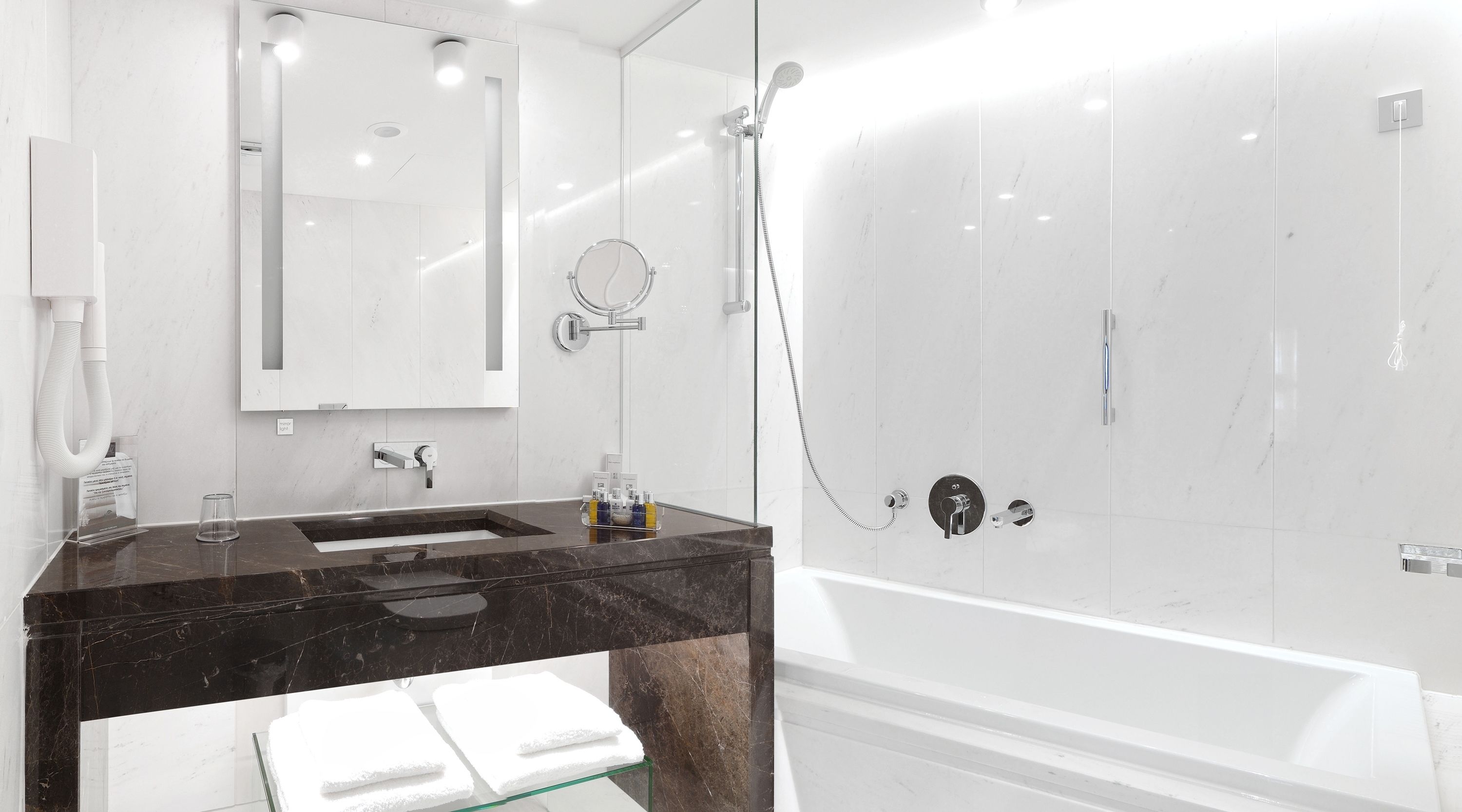 Un baño moderno con lavamanos de mármol, un espejo grande, ducha con cerramiento de vidrio y bañera blanca.