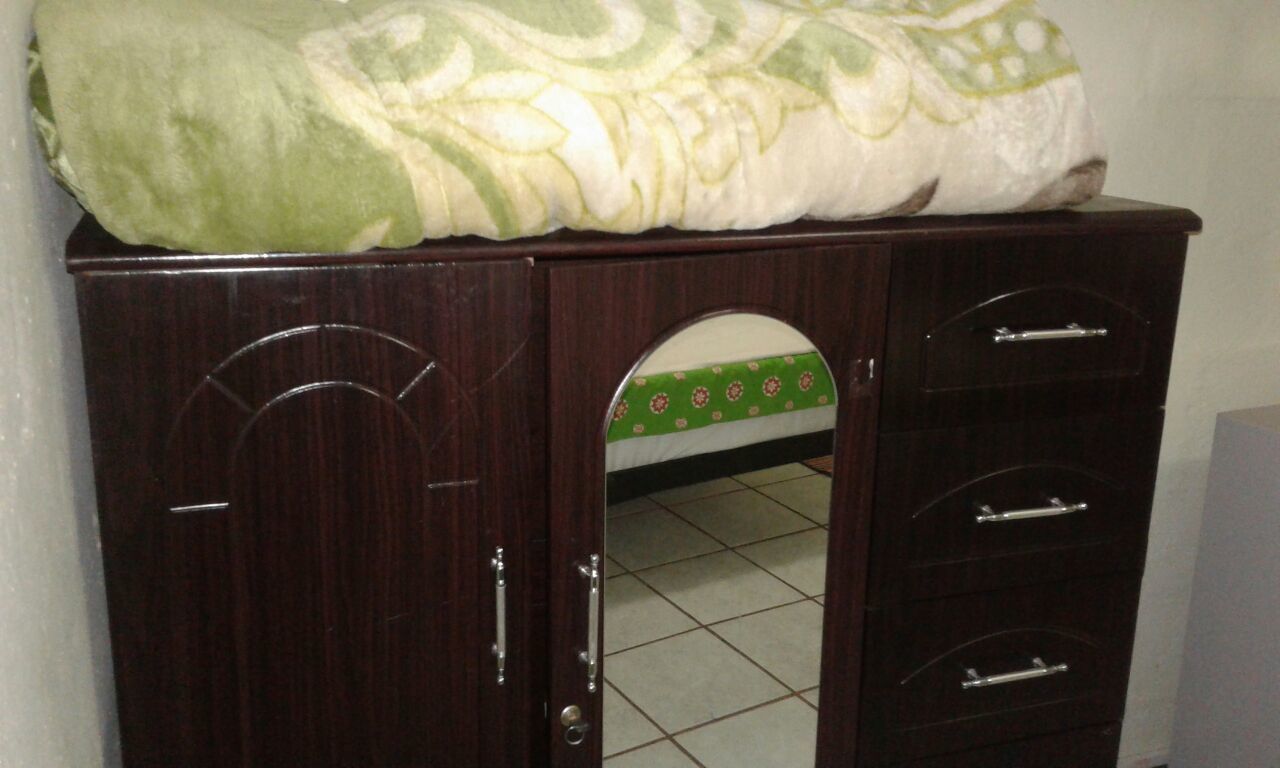 Un armario de madera con puerta espejada y un paño verde estampado en la parte superior.