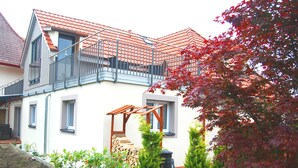 A two-story house with a red-tiled roof, a balcony, and a garden with various plants and a wooden pergola. - Bed & Breakfast Comfort House Olten - Lostorf (Lostorf)