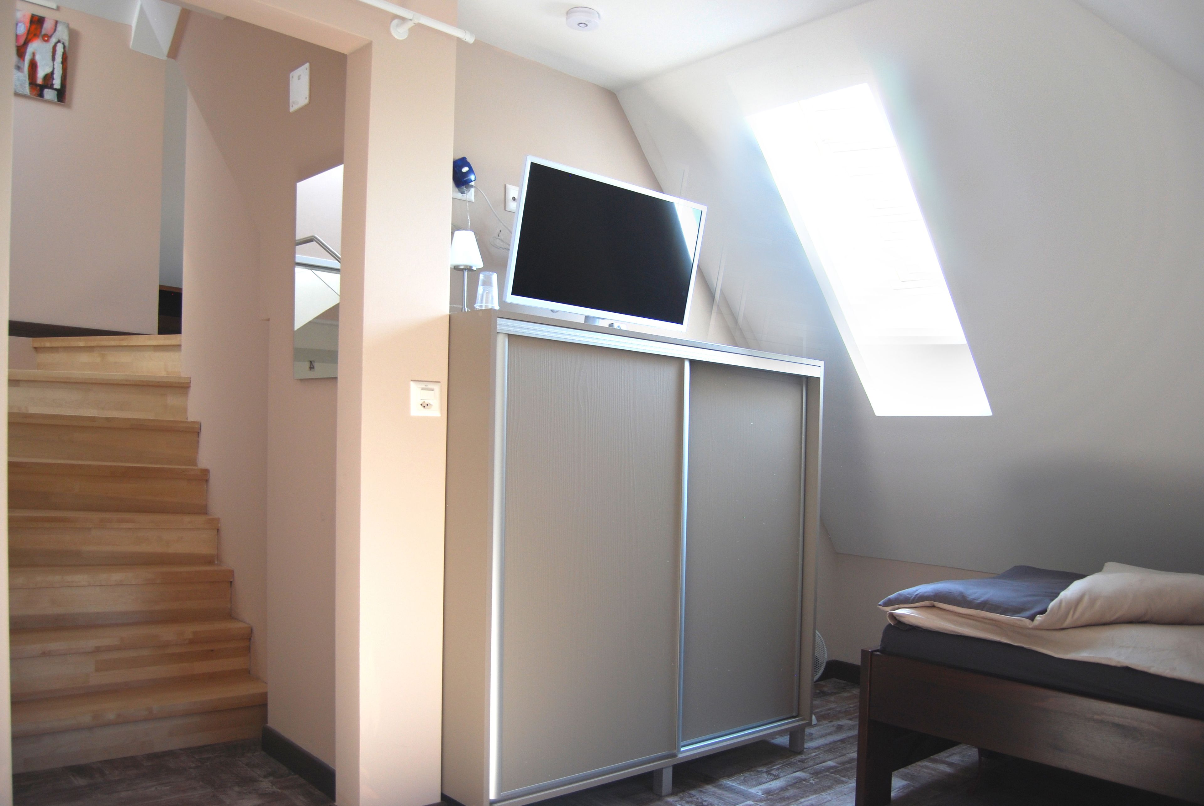 A bedroom with a bed, a TV on a cabinet, a staircase, and a skylight.