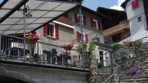 A building with a stone staircase leading to a balcony with red shutters. - Osteria Anzonico (Faido)