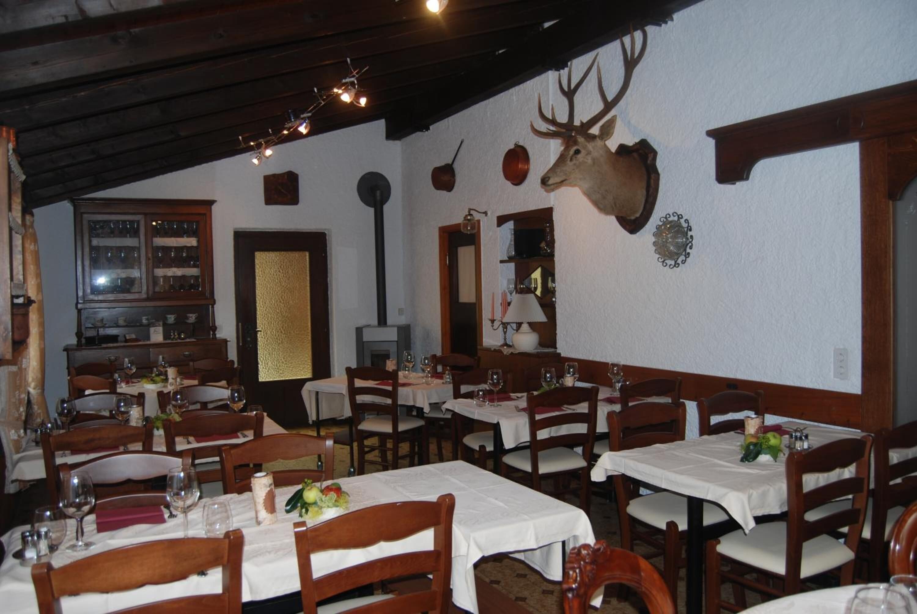 Ein Restaurant mit Holztischen und -stühlen, einem aufgehängten Hirschgeweih an der Wand und traditioneller Einrichtung.