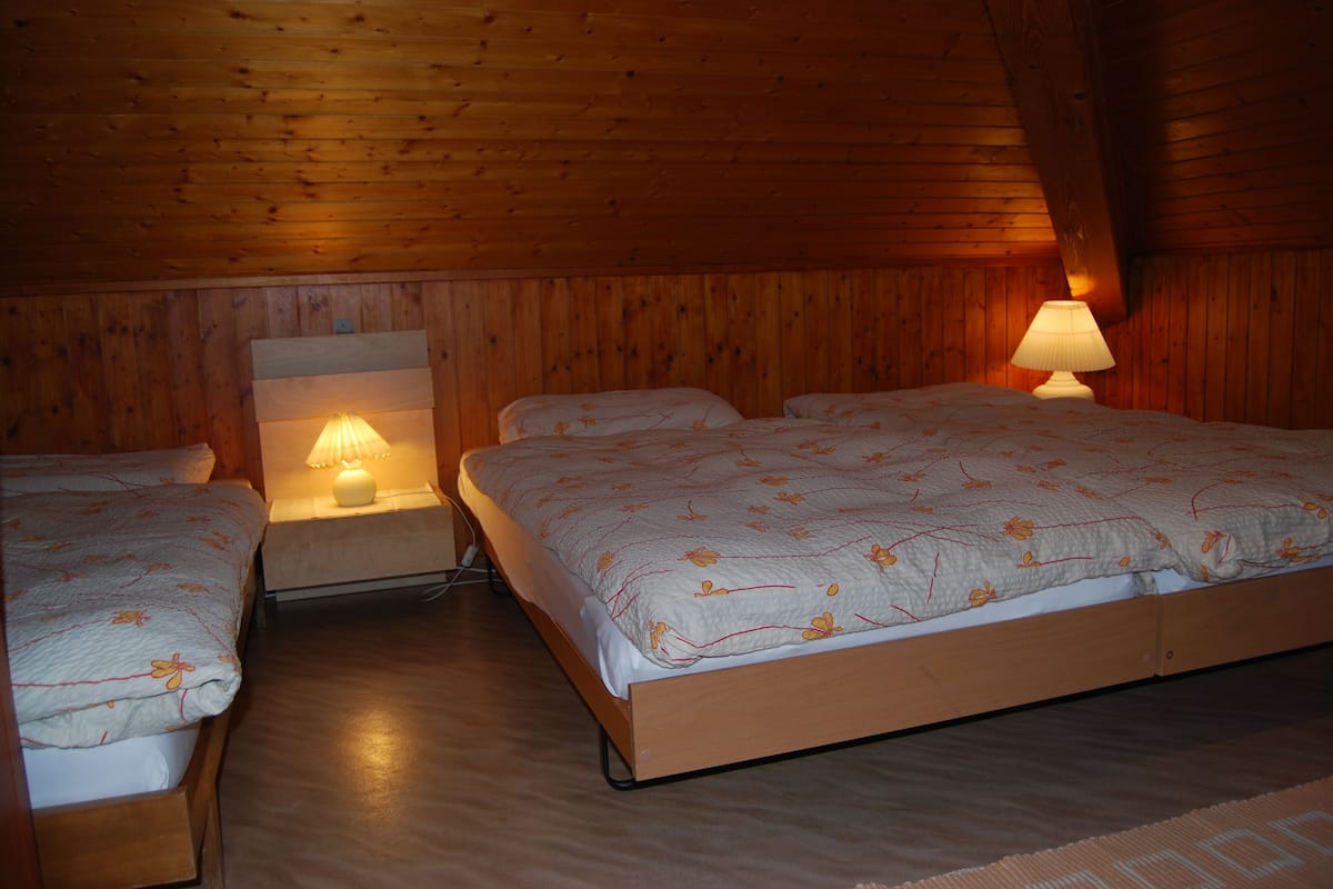 Ein gemütliches Schlafzimmer im Dachgeschoss mit zwei Einzelbetten und einem größeren Bett, Holzwänden und einer warmen Lampe.
