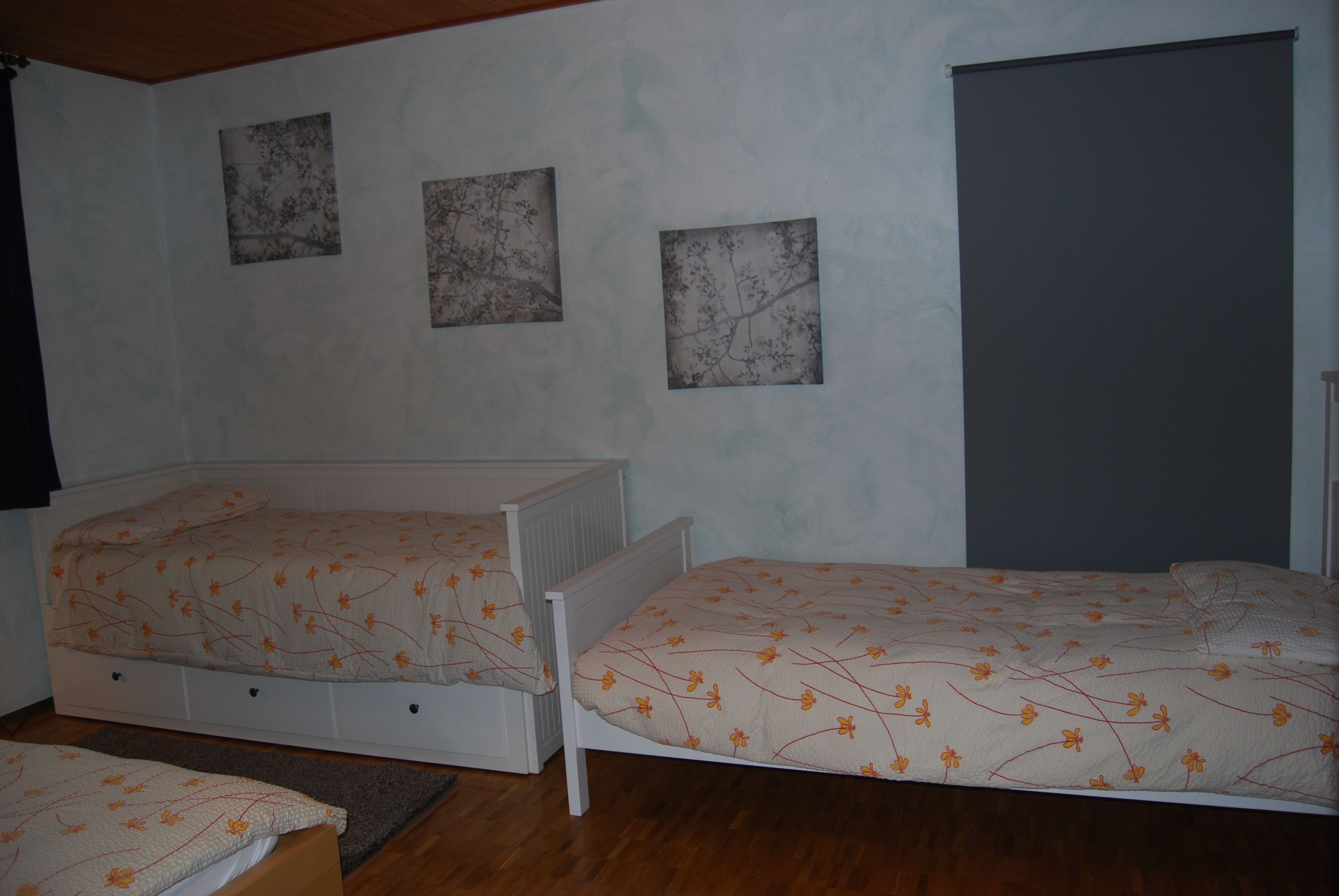 A bedroom with two single beds, a radiator, and three framed pictures on the wall.