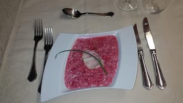 En tallerken rød risotto med pynt, bestik og et glas vand på et bord.