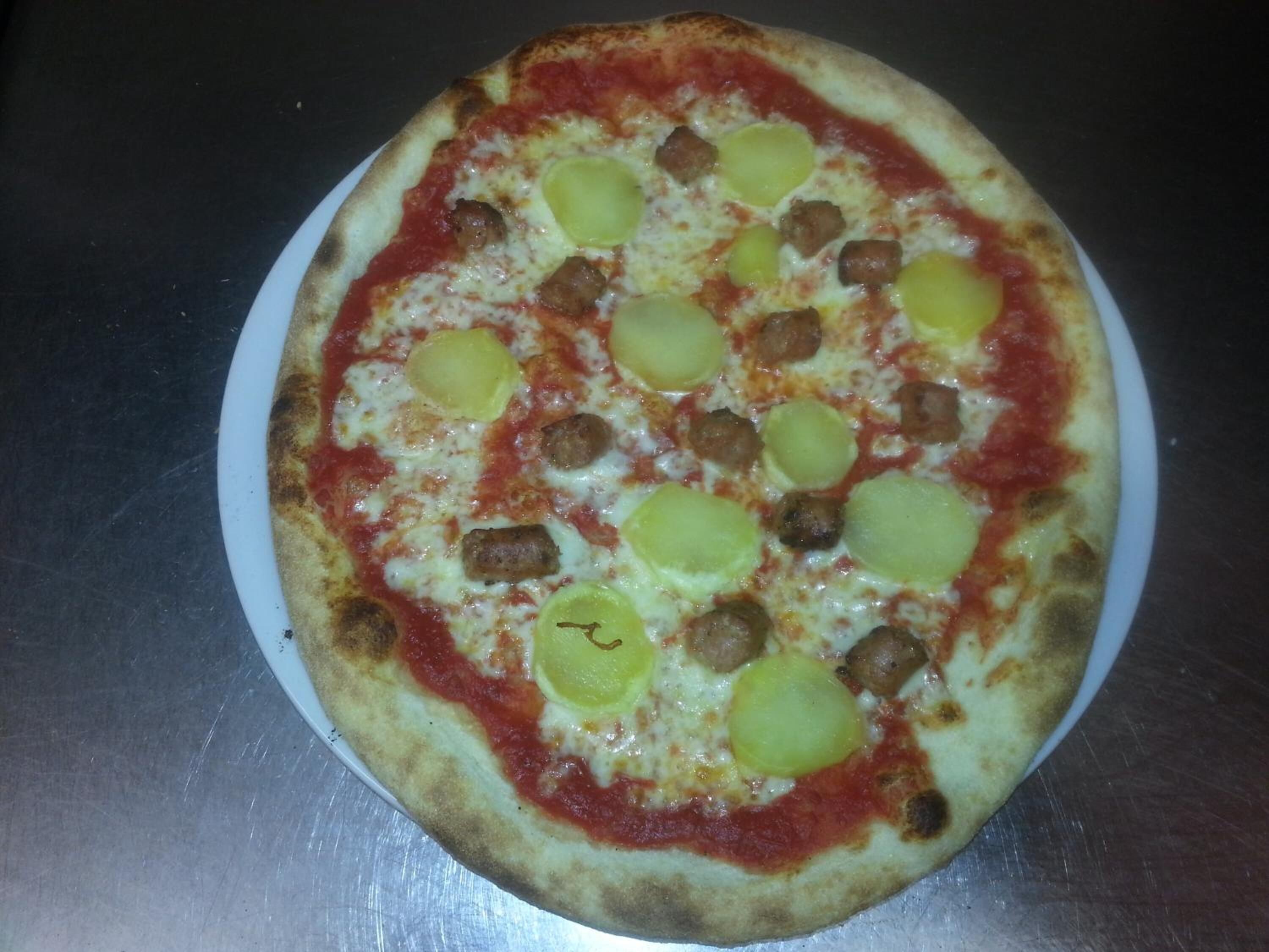 A pizza with sausage and green toppings on a white plate.
