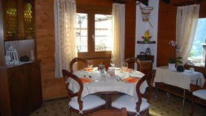 A wooden dining room with a table set for four, wooden chairs, and a window with curtains. - Osteria Anzonico (Faido)