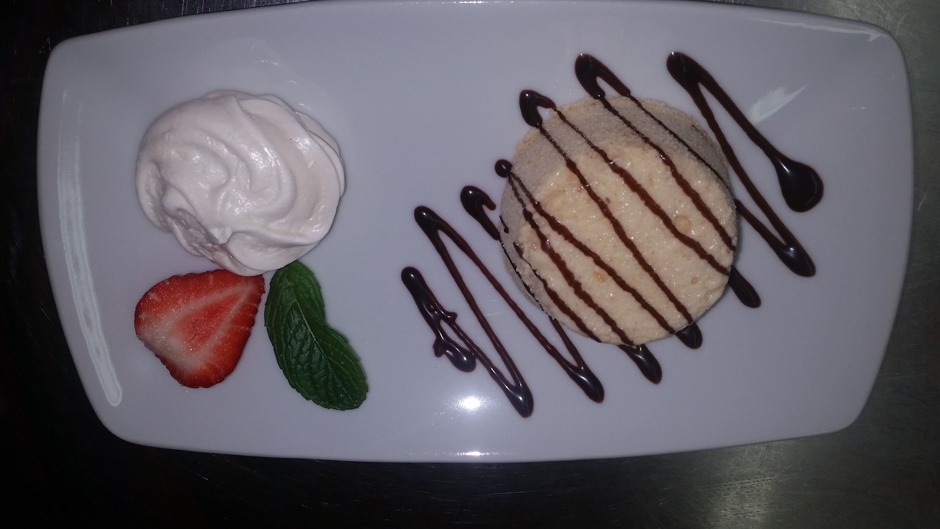 Un plato de postre con una bola de helado, una fresa y una hoja de menta.