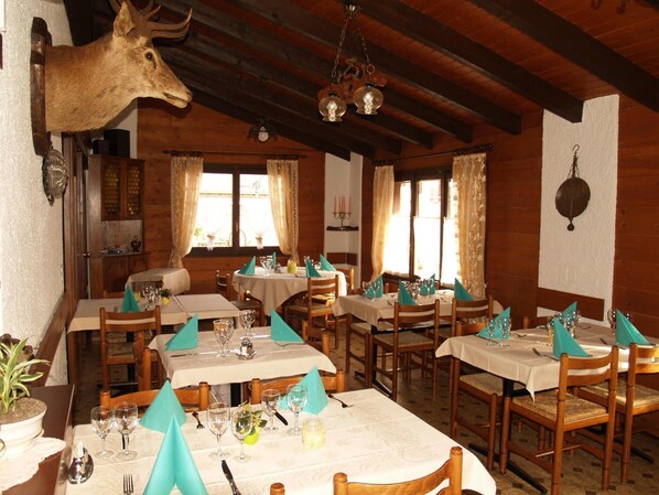 A restaurant with wooden interiors, multiple dining tables set with white tablecloths and turquoise napkins, and a mounted deer head on the wall. - Osteria Anzonico (Faido)