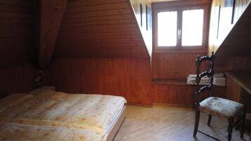 Un dormitorio con techo inclinado de madera, una cama con colcha floral, una silla con cojín floral y una ventana con vista al exterior.