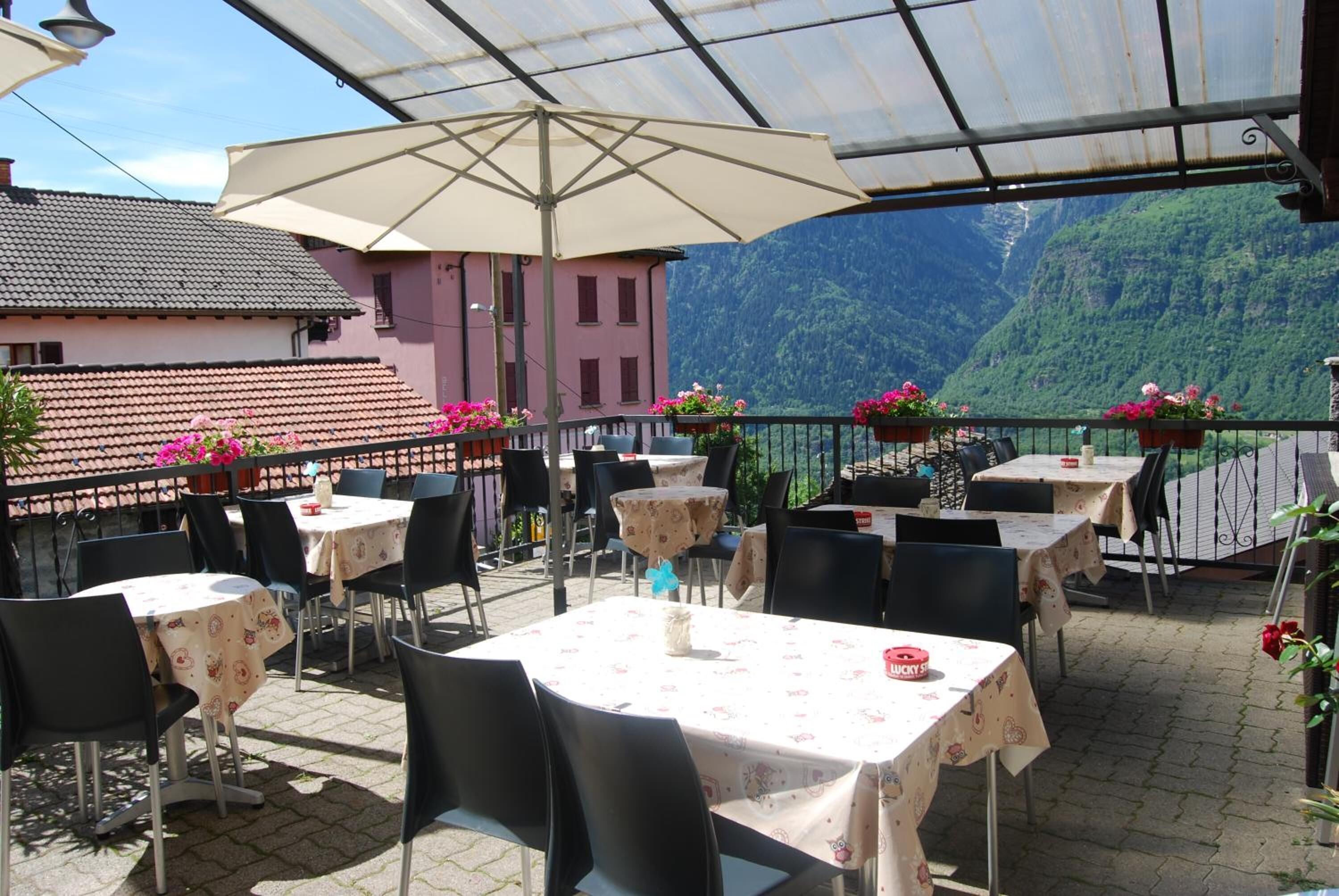 Une terrasse extérieure avec des tables et des chaises, un grand parasol et une vue sur une montagne.