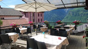 Eine Terrassengaststätte mit Tischen, Stühlen und einem großen Sonnenschirm, mit Blick auf einen Berg.