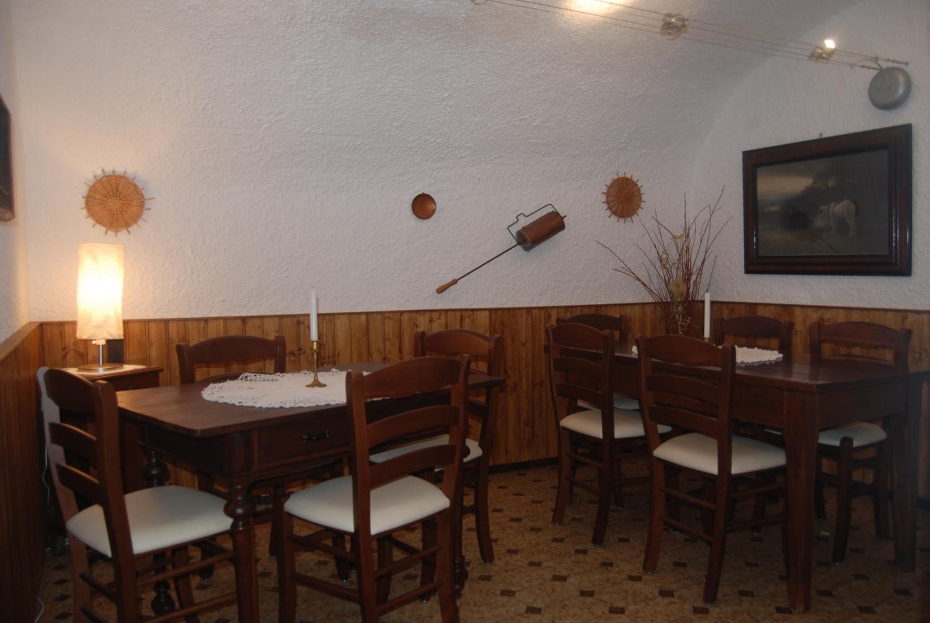 Un comedor con una mesa y sillas de madera, una lámpara fijada a la pared y un cuadro enmarcado.