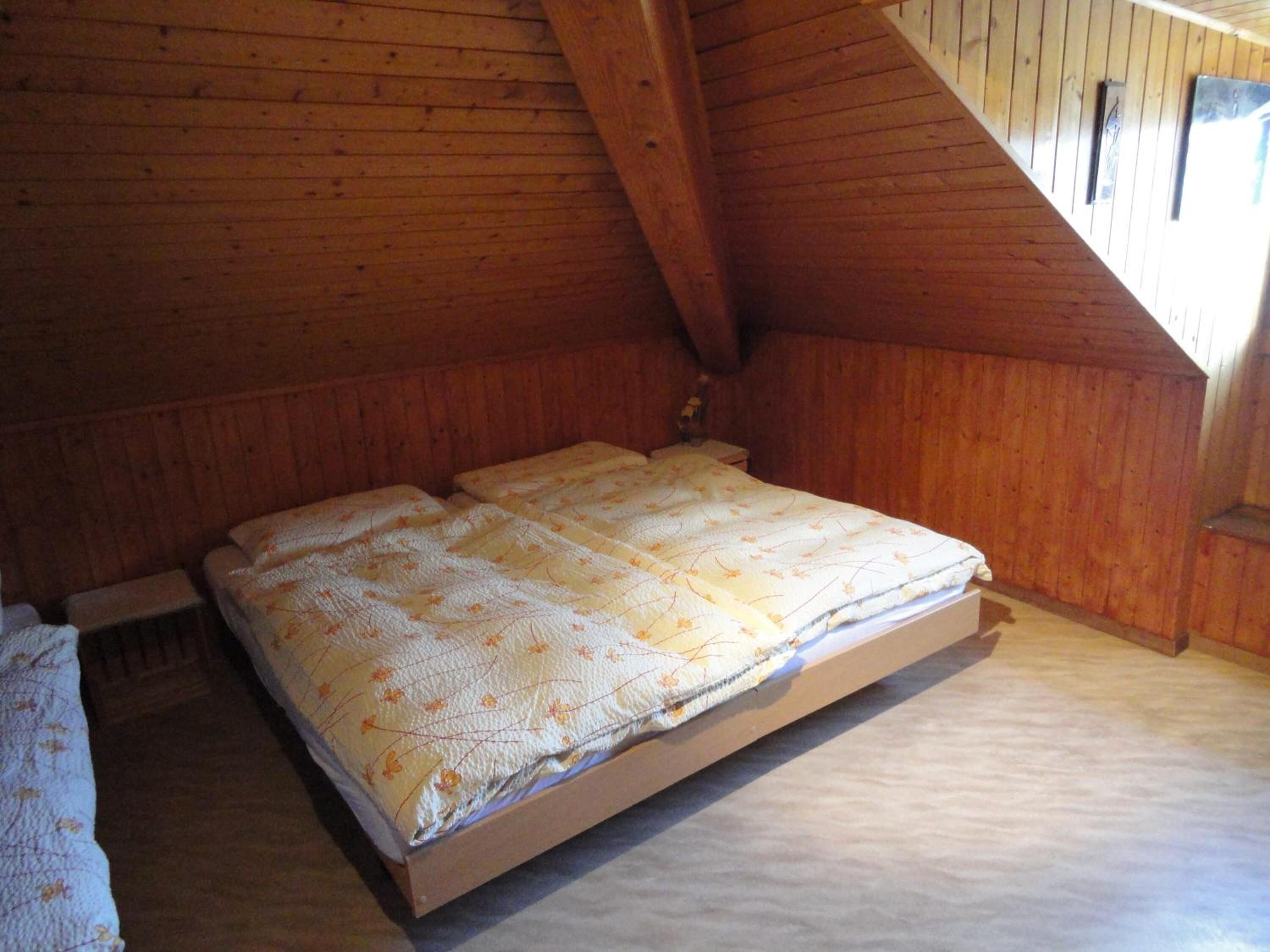 A wooden loft bedroom with a simple bed and a bench.