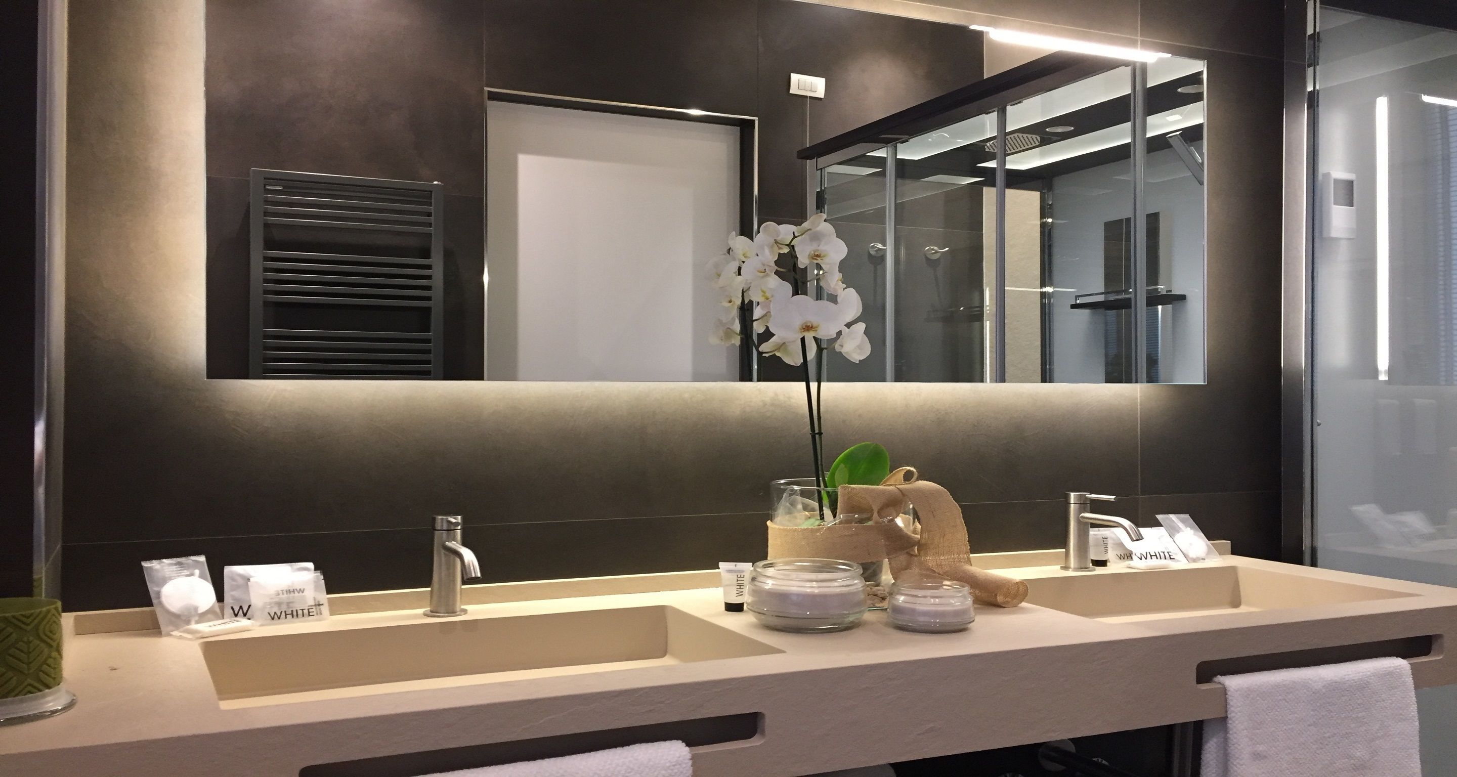 A modern bathroom with two sinks, a large mirror, and a potted orchid.