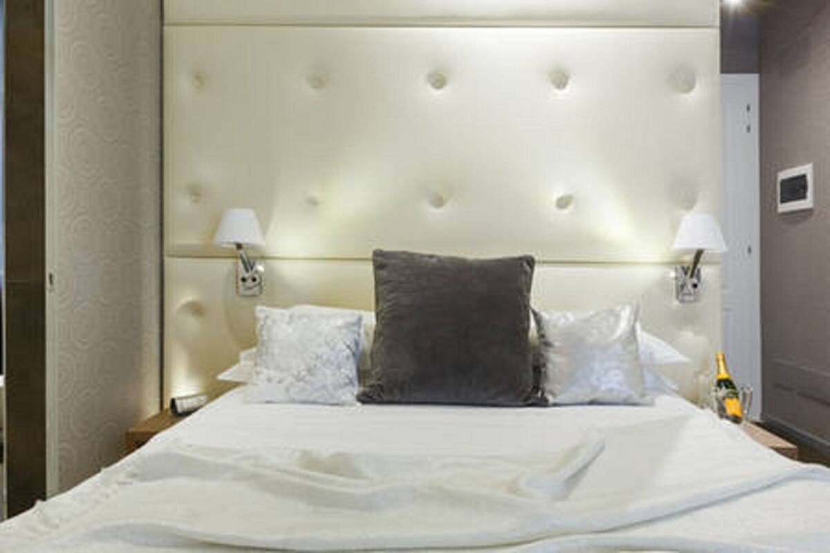 A neatly made bed with a tufted headboard, two bedside lamps, and a bottle of champagne on the nightstand.