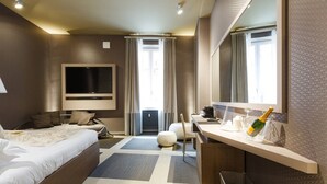 A modern hotel room with a large bed, a desk with a computer, a TV, and a minibar. - Private Luxury Suite (Rome)
