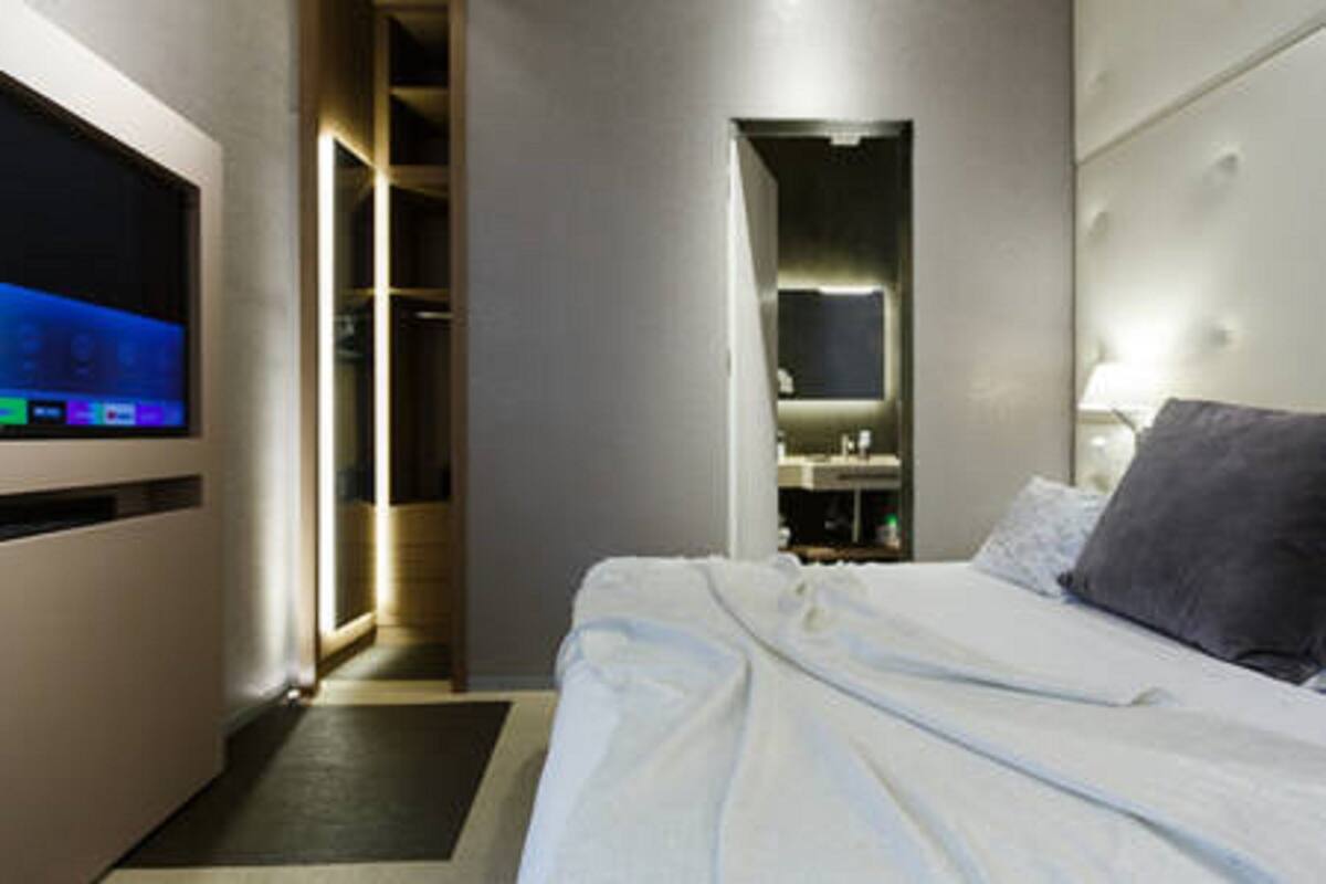 A hotel room with a bed, a TV, a mirror, and a bathroom visible through an open door.