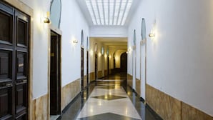 A hotel corridor with a polished floor, wall-mounted lights, and a ceiling with a grid pattern. - Private Luxury Suite (Rome)