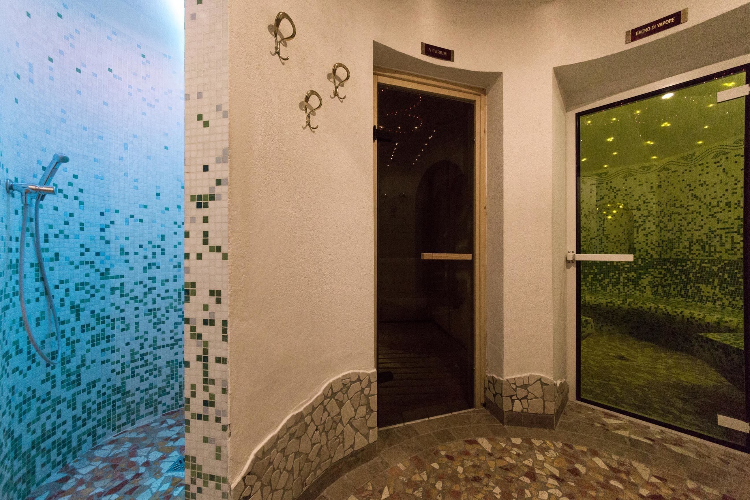 Een badkamer met betegelde muren, een douchegedeelte en een glazen deur die leidt naar een kamer met uitzicht op een groen landschap.