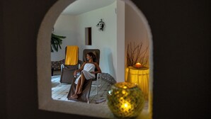 Una habitación con un espejo que refleja a una persona sentada en una silla, una mesita con una vela y un jarrón decorativo.