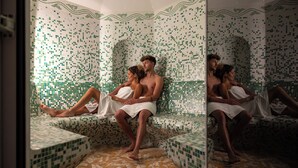Un baño con espejo, paredes y suelo de mosaico, bañera y zona de ducha.