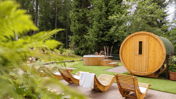 Una sauna de madera con puerta, rodeada de tumbonas de madera y un pequeño jacuzzi.