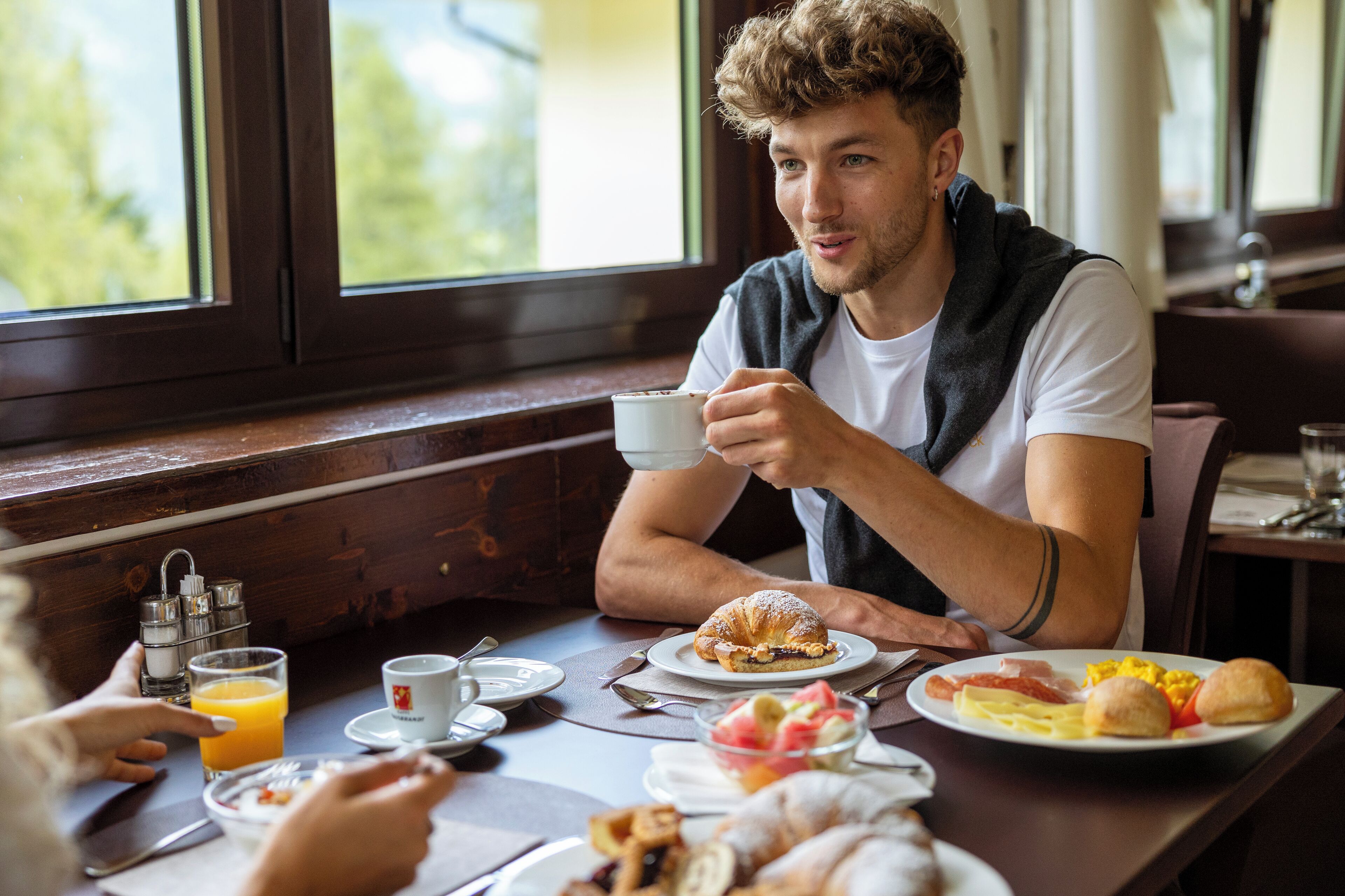 A breakfast setting with a table set for two, including plates with eggs, pastries, and a glass of orange juice.