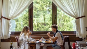 Una mesa de comedor con vistas a la vegetación a través de una ventana, una vela y una taza roja.