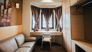 A compact room with a desk, a chair, a sofa, and a hanging coat rack. - Kertih Damansara Inn (Kerteh)