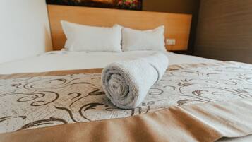 A neatly made bed with a rolled towel, a patterned bedspread, and a painting on the wall.