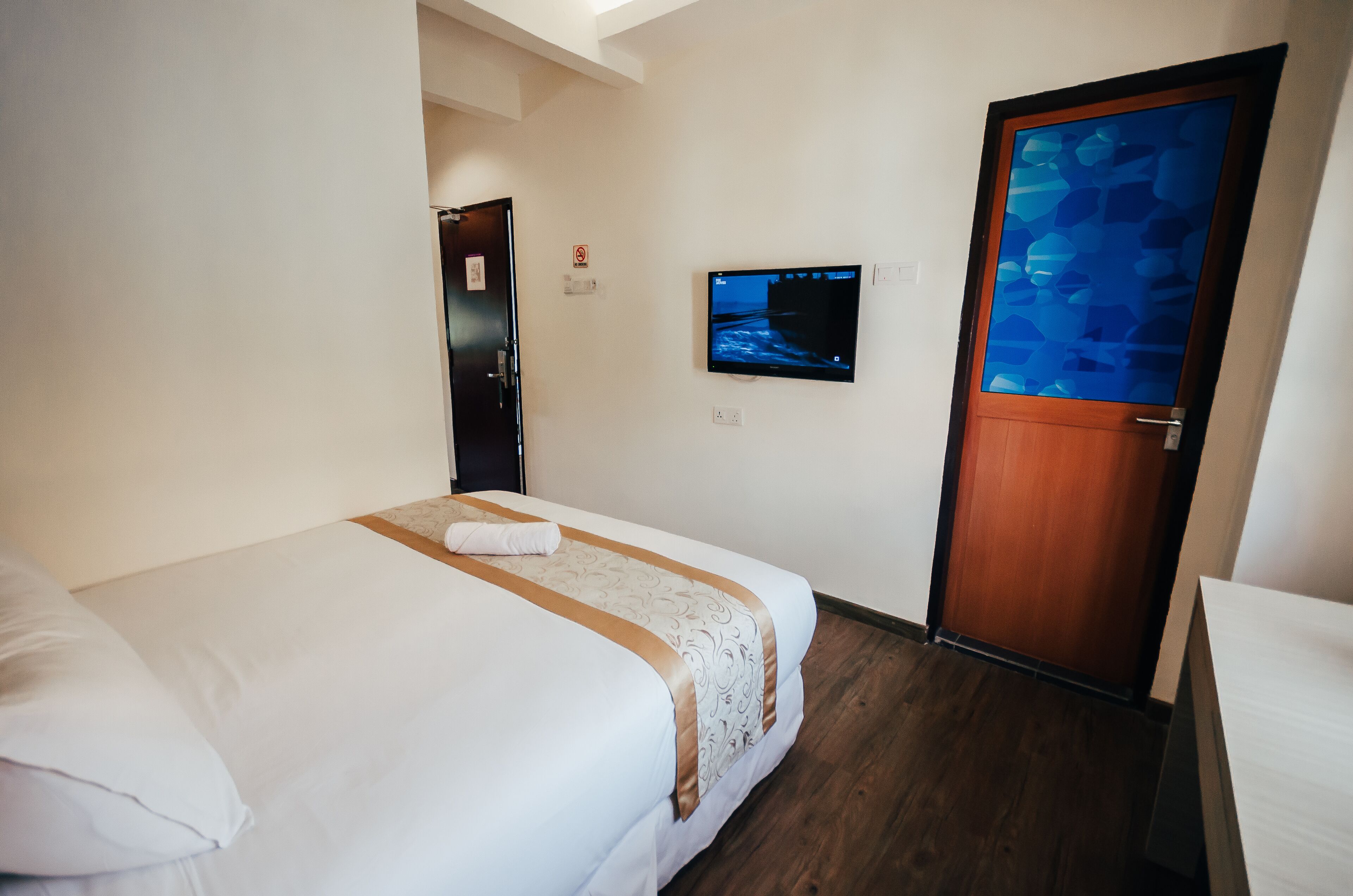 A hotel room with a bed, a television mounted on the wall, and a wooden door.