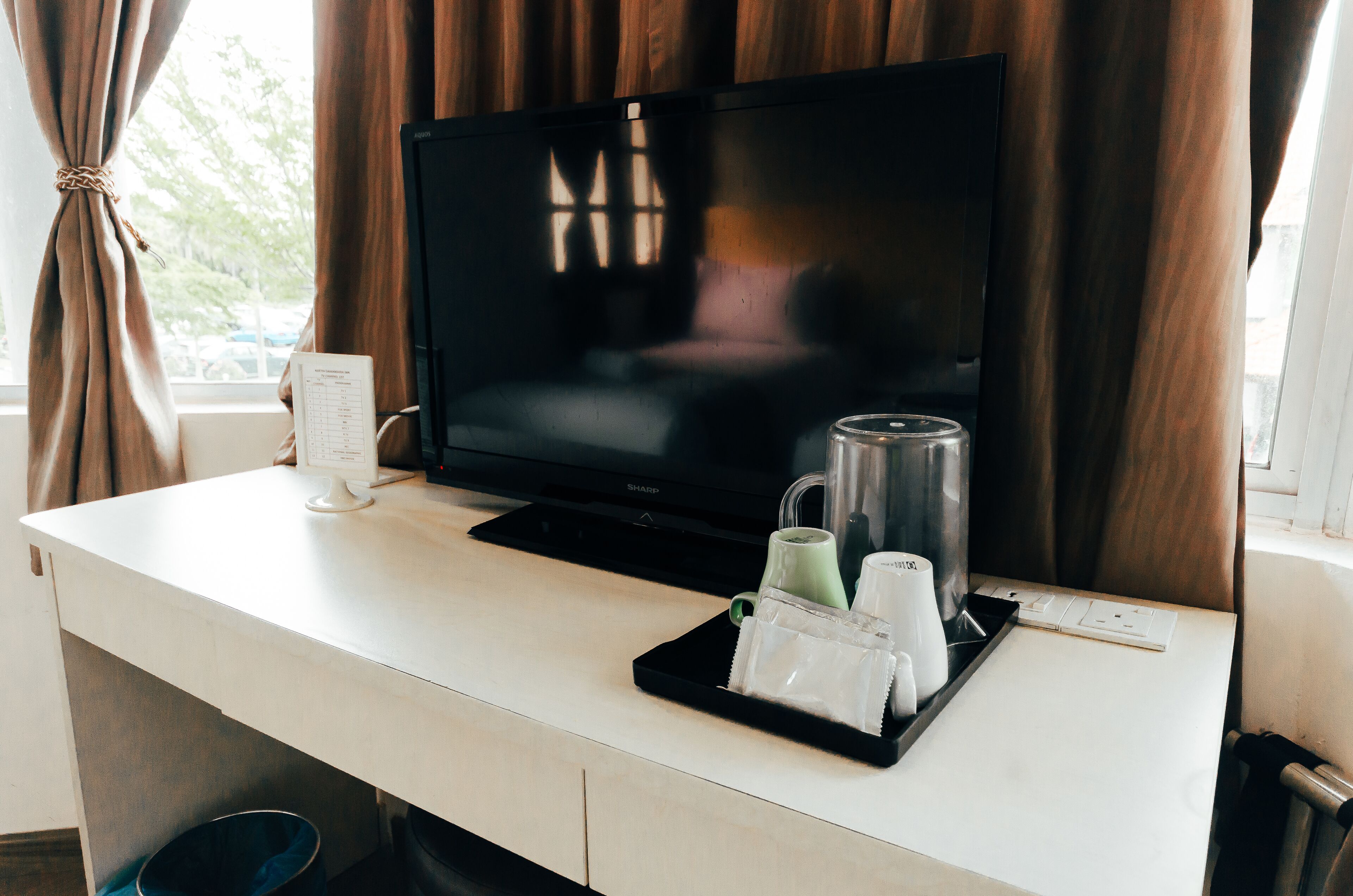 Een hotelkamer met een televisie, een koffiezetapparaat en een dienblad met kopjes en een glas.