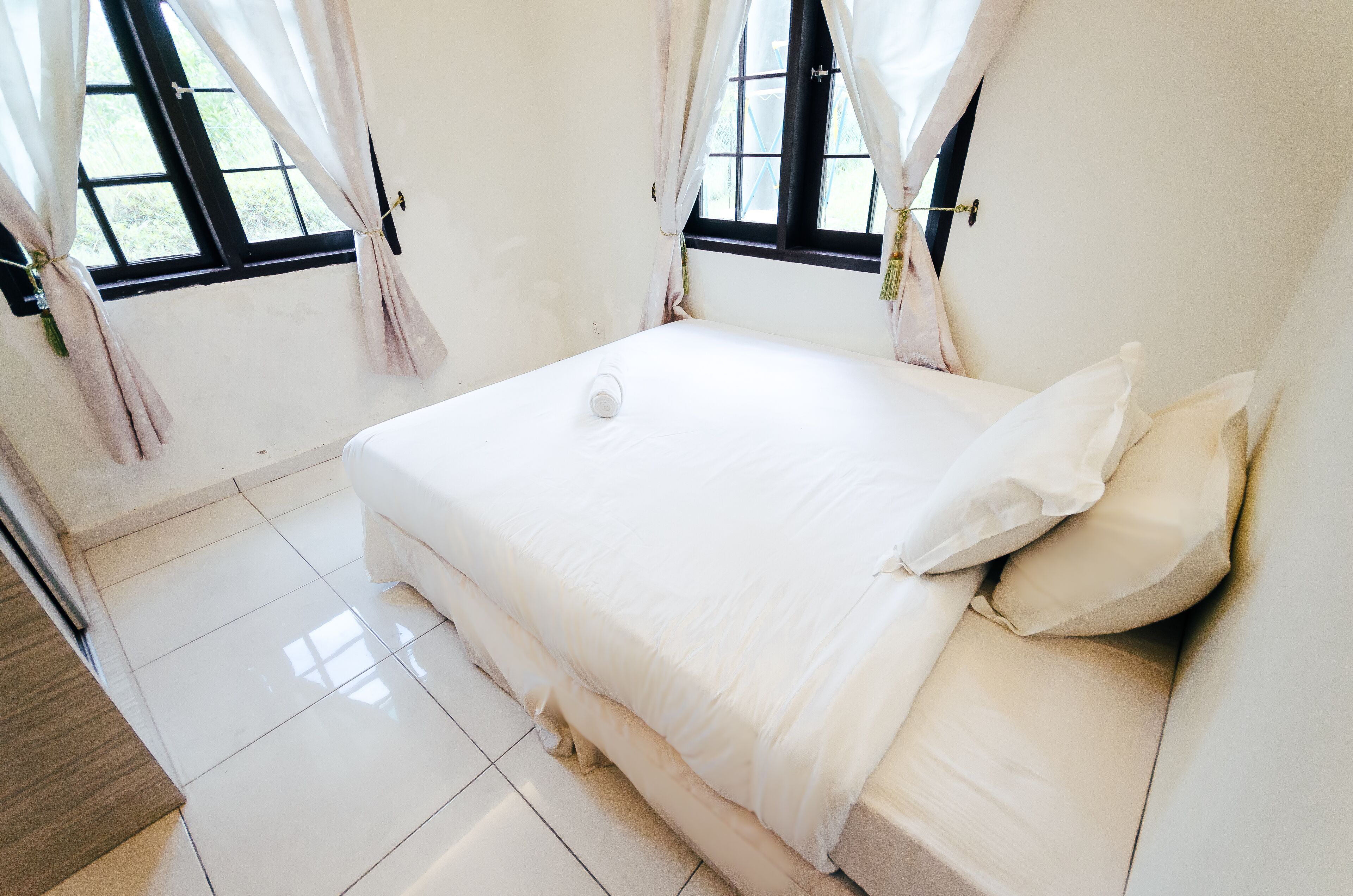Un dormitorio limpio y minimalista con una cama grande, cortinas blancas y vistas al exterior.