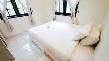 A clean, minimalist bedroom with a large bed, white curtains, and a view through the window.