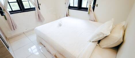 Un dormitorio limpio y minimalista con una cama grande, cortinas blancas y vistas al exterior.