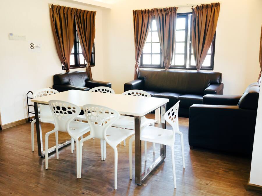 A room with a dining table and chairs, a sofa, and two windows with curtains.