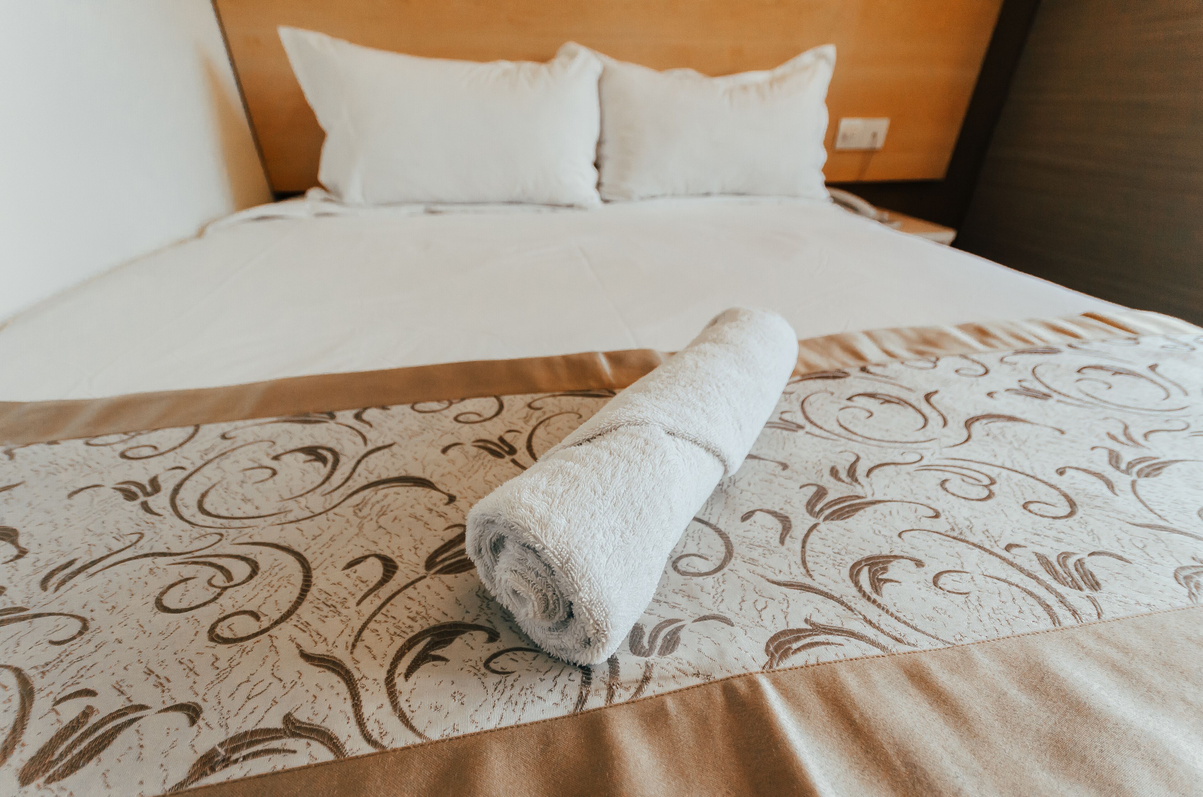 A neatly made bed with a rolled towel on the bedspread.